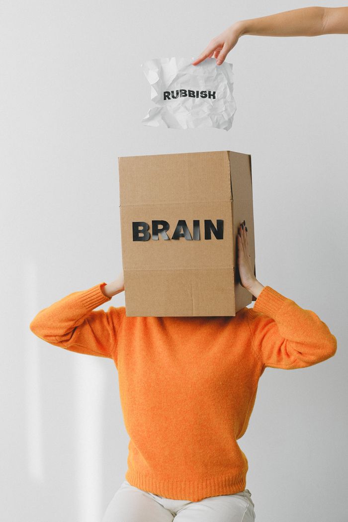ours-journey Crop person putting creased paper with Rubbish title in container with Brain inscription on head of female on light background